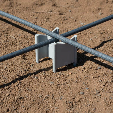Gray rebar support holder on dirt with two steel rebars crossing for concrete reinforcement.
