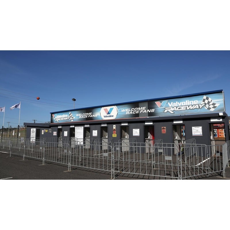 Valvoline Raceway entrance with fences, bright blue sky, welcoming fans, outdoor race event.